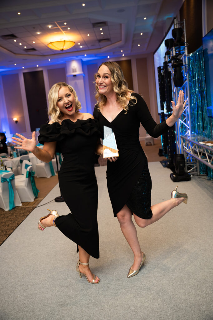 Amy Eley and Roisin sparkle on stage with the Creative Business of the Year award, radiating energy and giving full razzle dazzle at the 2025 Devon Chamber Business Awards.